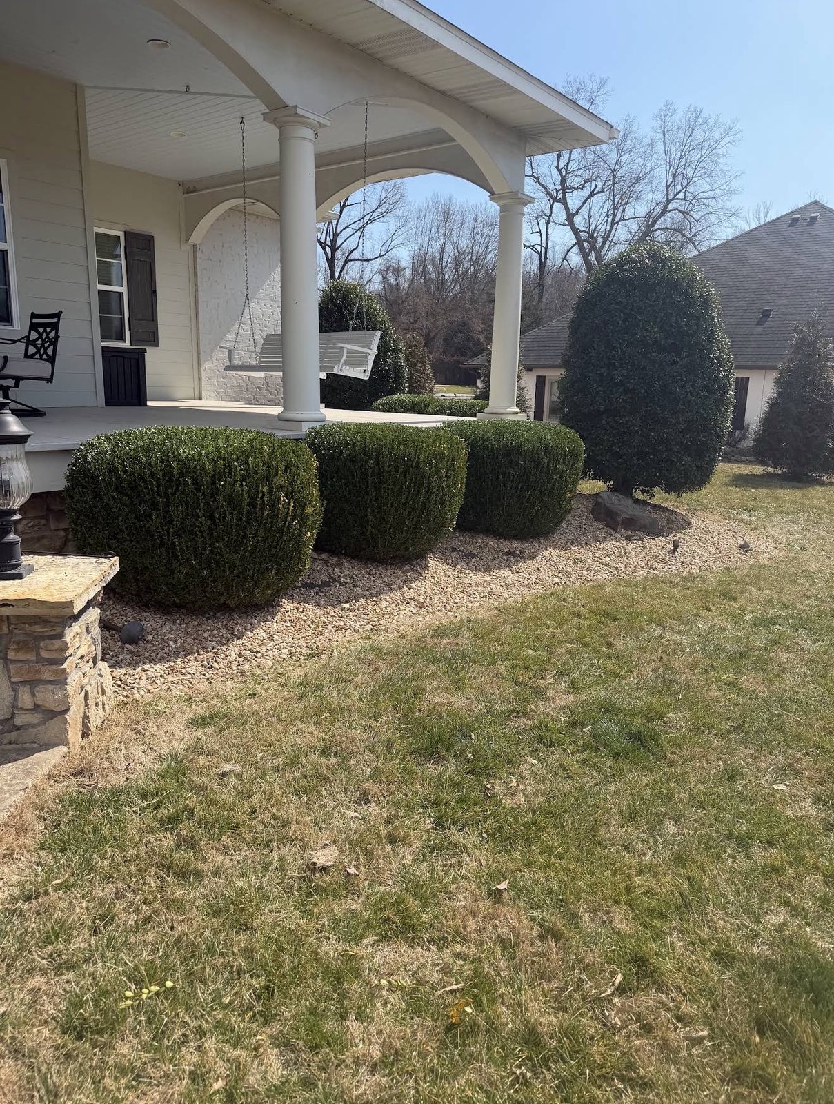 Trimmed boxwoods and a cleared gravel bed along a front porch