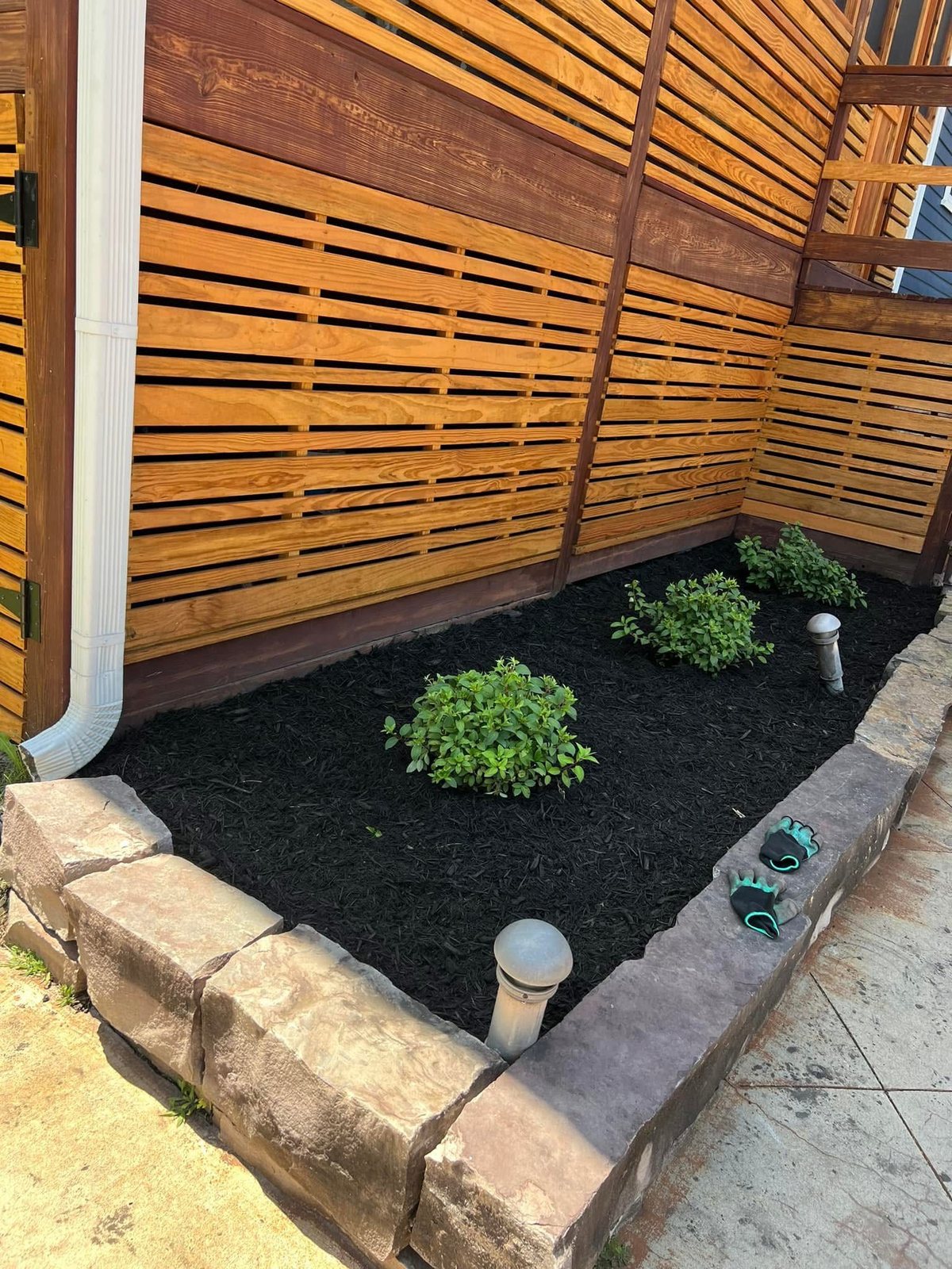 Fresh dark mulch spread in a stone-edged bed beside a slatted fence
